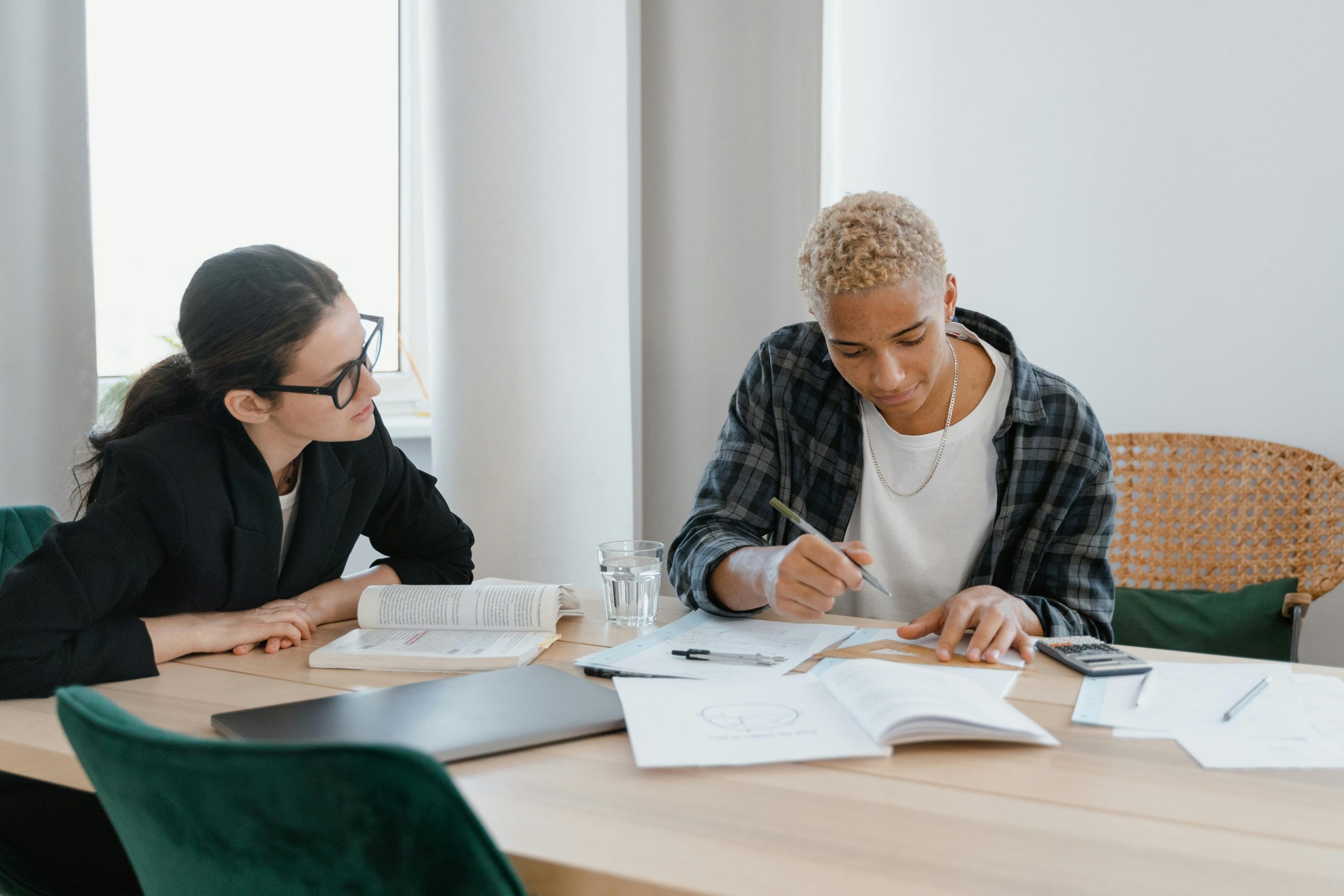 Two adults engaged in a focused study session at a home table with books and papers.